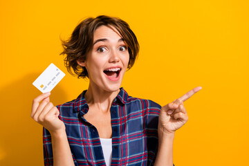 Aufkleber - Portrait of excited ecstatic girl wear plaid shirt show debit card directing at sale empty space isolated on yellow color background
