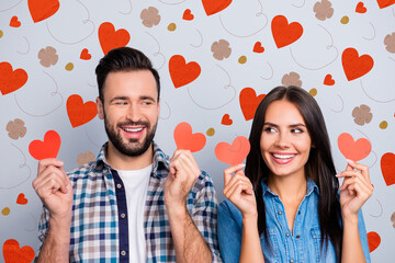 Aufkleber - Love story of sweet, cheerful, positive, smiling couple in shirts showing small red paper hearts in two hands, looking to each other with eyes over grey background