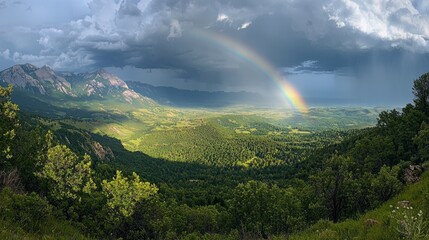 Aufkleber - A stunning rainbow stretches across the sky, illuminating a lush green valley surrounded by towering mountains. Dark clouds gather, hinting at an imminent storm while sunlight breaks through