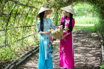 Two young Vietnamese women in traditional Ao Dai dress holding flower basket in garden