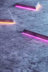 Poster - Colorful neon lights illuminate geometric shapes laid out on a textured concrete surface. This artistic display adds a modern touch to the indoor environment, enhancing visual interest