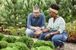 © Seventyfour - Adult male client choosing coniferous shrubs for garden project with African American female landscape architect, while sitting on squat and discussing design options in plant nursery