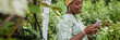 © Seventyfour - Website header shot of positive African American female landscape designer writing message on mobile phone communicating with clients while working in green garden