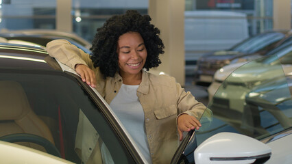 Wall Mural - Happy customer client African American woman businesswoman girl buying new car enjoy luxury purchase in auto dealership female owner buy rent vehicle modern electric automobile looking camera laughing