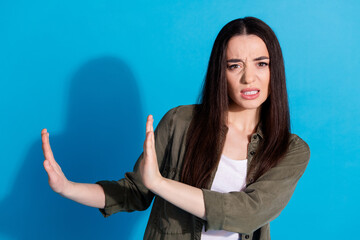 Wall Mural - Young woman showing a gesture of disapproval against a blue background, expressing negative emotions and signaling stop with open hands.