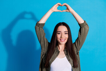 Wall Mural - Young woman making a hand heart gesture on a blue background with a cheerful expression