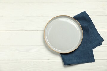 Wall Mural - Blue napkin and empty plate on white wooden table, top view. Space for text