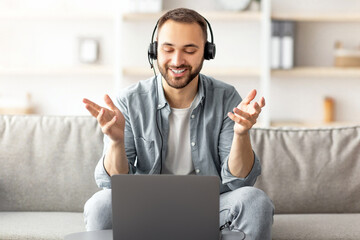 Poster - Happy young guy in headset making video call on laptop at home, talking to camera. Young Caucasian man enjoying online communication, participating in web conference or business meeting