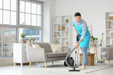 Poster - Young man in apron vacuum cleaning carpet at home