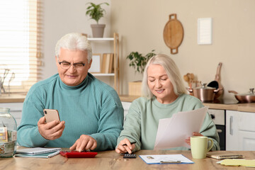 Wall Mural - Senior couple with mobile phone calculating utility bills in kitchen