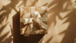 © Mutshino_Artwork - A beautifully wrapped gift box with floral-patterned paper and a satin ribbon, placed in warm sunlight with soft leaf shadows
