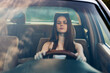 © SHOTPRIME STUDIO - Young woman with long hair driving a car, focused and calm expression, in a sunlit interior, emphasizing freedom and independence, with a soft color palette.