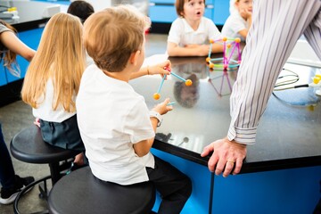 Poster - Children in a science class, sitting at a table, engaged in a hands-on activity with colorful models. Teacher nearby, guiding the science lesson. Science teacher teaching school kids.