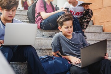 Fototapete - Group of boys using laptops and tablets on stairs. Boys with laptops, boys with tablets, boys studying. Young boys, technology, learning. Boys, laptops, tablets. High school boys with laptops.