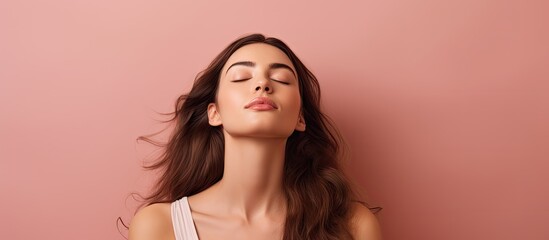 Canvas Print - Serene young woman with long brown hair wearing a white top against a soft pink background, eyes closed, exuding calm and tranquility.