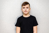 Portrait of a ten year old boy against a grey wall in a black T-shirt.