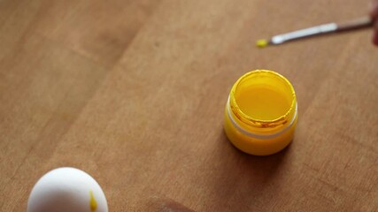 Wall Mural - a child dips a brush into a jar of yellow paint. girl painting eggs for Easter