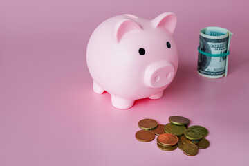 Wall Mural - A piggy bank in the form of a pink pig, small coins and hundred dollar bills on a pink background. The concept of savings and investments.