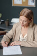 © TrueFrame Collective - Blond mature woman in elegant suit holding pen over contract before putting her signature after negotiation