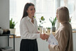 © TrueFrame Collective - Young successful businesswoman shaking hand of mature female colleague while greeting her in office