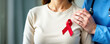 © Yelizaveta - Banner close-up doctor in a blue uniform put his hand on the shoulder of a woman in a beige long sleeve with a red ribbon on her chest, concept world cancer day, world aids day