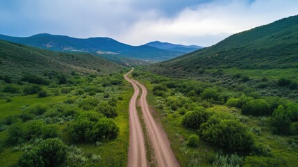 Aufkleber - Scenic Dirt Road Curving Through Verdant Green Valley Surrounded by Mountains Under Cloudy Sky