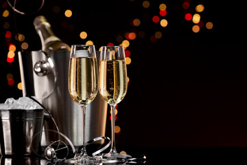 Champagne in glasses, bottle and ice buckets on mirror surface against color background with blurred lights, space for text