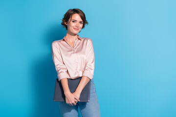 Poster - Young woman with bob haircut in pink satin blouse stands elegantly against a blue background holding a laptop