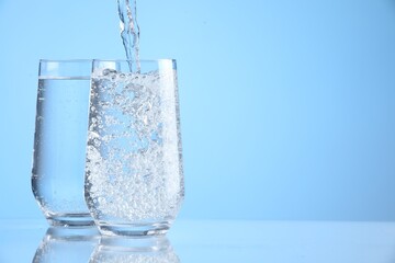 Wall Mural - Pouring refreshing soda water into glasses on light blue background, closeup. Space for text