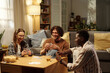 © TrueFrame Collective - Happy intercultural friends playing cards at leisure while gathered around table in spacious living room