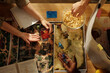 © TrueFrame Collective - Top view of hands of three young intercultural friends playing tabletop game by table and having popcorn