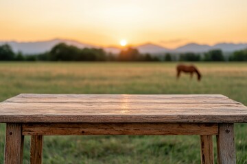 Poster - Empty wooden table with blurred field, horse, and mountains at sunset in the background, creating a peaceful nature-inspired setting