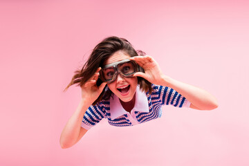 Wall Mural - Laughing young woman with stylish brunette bob and goggles on pink background