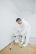 © DSMT - Renovation of the premises. A young man with dark hair paints the wall white in the apartment. He holds a roller in his hands. The concept of cheap repairs.