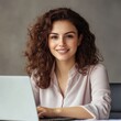 © Nica - Elegant corporate woman with curly brown hair, wearing a stylish pastel blouse, sitting at a sleek desk with a laptop, warm office lighting, subtle smile, modern and minimalist workspace