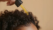 © Alla Bondaruk - A close-up of a hand applying oil to curly hair against a beige background, capturing a moment of self-care and nourishment, hair serum