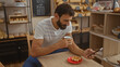 © Krakenimages.com - Young man with a beard enjoying coffee and pastry while using his phone in a cozy bakery.