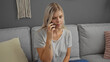 © Krakenimages.com - Young blonde woman at home sitting on a couch in a living room talking on the phone looking serious and thoughtful