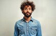 © miss irine - Young man with curly hair and beard poses for photo. He wears a denim shirt and makes a funny face. Studio portrait of a casual man. Light gray background. Attractive and photogenic.