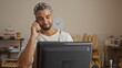 © Krakenimages.com - Young man with beard working in a bakery shop, talking on phone with computer monitor in foreground and shelves of bread and pastries in the background, wearing apron.