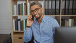 © Krakenimages.com - Young, arab, handsome man with a beard talking on the phone at his office desk surrounded by shelves of files and books