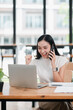 © Satori Studio - A joyful young woman celebrates success on a phone call while working on her laptop in a bright, modern office setting.