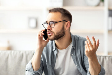 Poster - Stressed young freelancer using laptop and making call on smartphone at home office. Millennial Caucasian man overworking to meet deadline, having error in his project