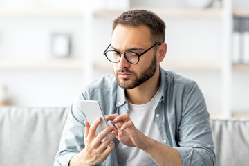 Poster - Serious young freelancer using laptop and smartphone at home office. Millennial Caucasian man working online, having business meeting on pc, communicating to coworkers remotely