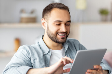 Poster - Cheerful young man using tablet pc, working or studying online from home. Portrait of positive Caucasian guy making business project, having video call or remote meeting indoors