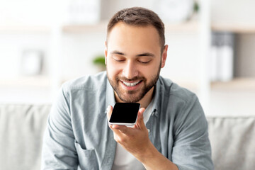 Poster - Cheerful millennial guy sitting on couch with cellphone at home, mockup for mobile app or website on screen. Young Caucasian man using modern gadget indoors. Contemporary technologies concept