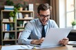 © velikiyzayats - Excited Young Man in Glasses Working on Laptop in a Cozy Home Office with Plants and Bookshelves in the Background