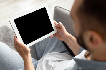 Poster - Unrecognizable young guy working on tablet computer with empty screen at home office, mockup for website or app design. Closeup of millennial man holding touch pad, space for advertisement