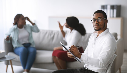 Wall Mural - Stressed black male psychologist and angry LGBT lesbian couple fighting during session at office, copy space. Homosexual spouses having conflict on consultation with psychotherapist, banner