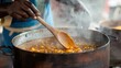 © EUT - A person stirs a large pot of steaming, orange stew with a wooden spoon. Perfect for blogs about food, cooking, or cultural traditions.